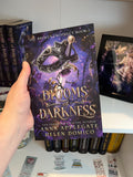 Book titled 'Blooms of Darkness' held by a hand with more books in the background.